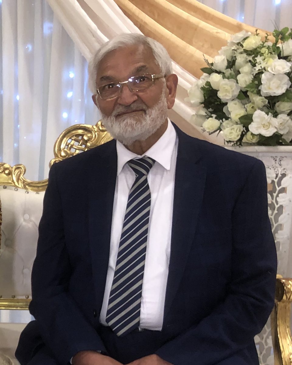 Mukhtar Ahmed, smiling, in a navy suit and striped tie